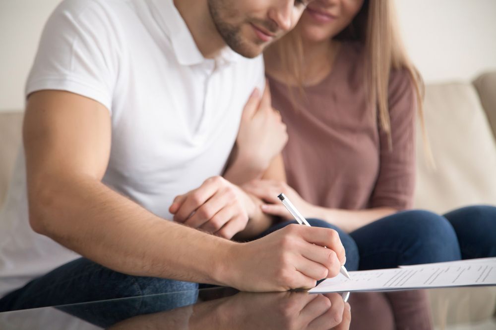 Man and woman sitting together on couch as man signs paper